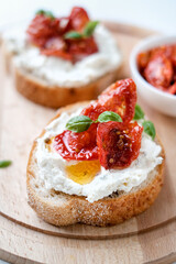 Two bruschettas with ricotta cheese, olive and dried tomatoes on ciabatta bread on white background. Olive oil and spices decorated. Copyspace.