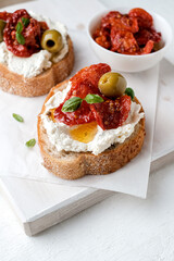 Two bruschettas with ricotta cheese, olive and dried tomatoes on ciabatta bread on white background. Olive oil and spices decorated. Copyspace.