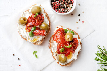 Two bruschettas with ricotta cheese, olive and dried tomatoes on ciabatta bread on white...