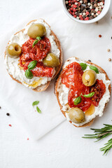 Two bruschettas with ricotta cheese, olive and dried tomatoes on ciabatta bread on white background. Olive oil and spices decorated. Copyspace.