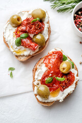 Two bruschettas with ricotta cheese, olive and dried tomatoes on ciabatta bread on white background. Olive oil and spices decorated. Copyspace.