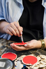 Obraz premium Process making handmade wooden Christmas toys in carpentry woodworking workshop. Hands of master paint round wooden surface red. Handmade. Small business concept.