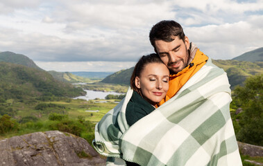 travel, tourism and love concept - happy smiling couple in warm blanket over river valley at Killarney National Park in ireland on background