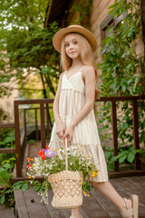 Dreamy tween girl with wildflower in basket standing on doorstep of country house