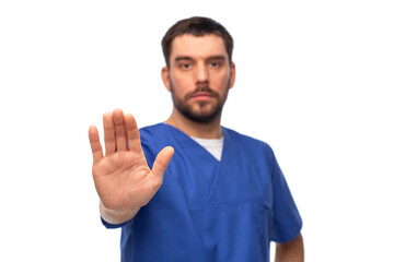 healthcare, profession and medicine concept - male doctor in blue uniform showing stop gesture over...