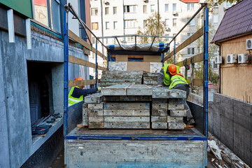 Professional builders in workwear and orange hardhats are unloading a truck with materials near a building under construction
