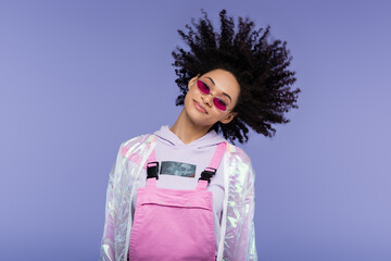 cheerful african american woman in pink sunglasses shaking head isolated on purple.