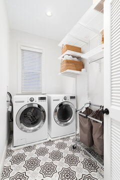 A Laundry Room With White Washer And Dryer, A Patterned Tile Floor, And Organized Shelving On The Wall.
