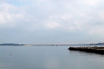 The breakwater in a bay with a long bridge in the background