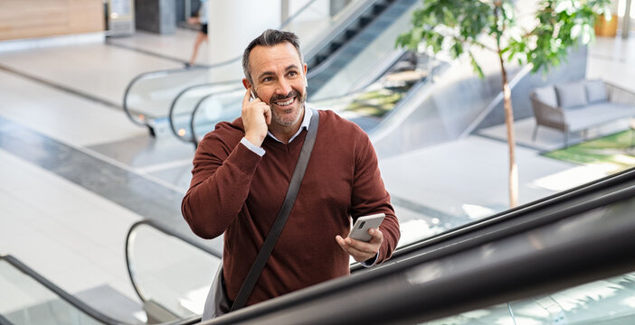 Mature businessman on escalator talking on smartphone
