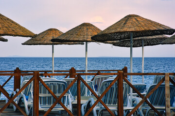 Empty sun loungers and beach umbrellas and wooden guards by the sea