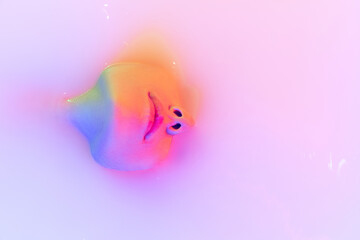 Closeup female face, young beautiful girl in milk bath with soft glow in blue-green neon light. Beauty, fashion, style, skincare concept