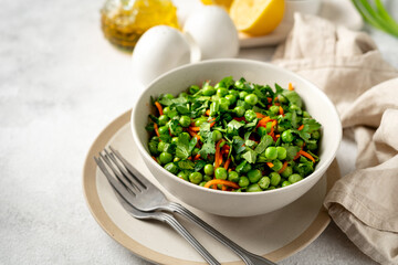 A bowl of salad with green peas, pickled carrots and parsley with olive oil on a bright kitchen table. Delicious healthy salad for health and weight loss closeup	