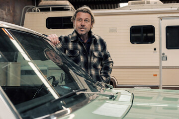 Blond man stands by his classic american muscle car in a winter storage.