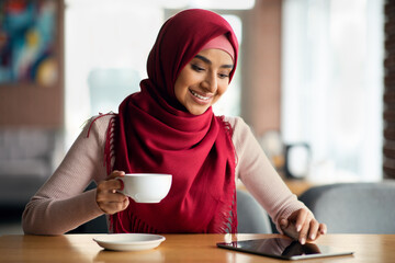 Woman in hijab chilling at cafe alone, using digital tablet