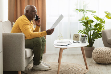 Senior African Businessman Talking On Phone Holding Paper Indoors, Side-View