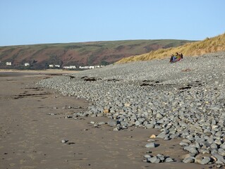 A group of people sitting on  Ynysalas beach in the winter sunlight, Ceredigion, Wales, UK.