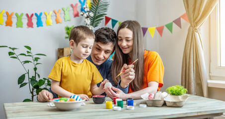 Mom, dad and child together are coloring eggs and having fun in a decorated room. Concept of family preparation for Easter, festive spring mood