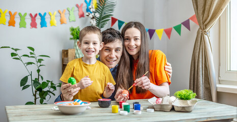 Family coloring Easter eggs in a decorated room. Mom, dad and child are having fun and preparing for the holiday
