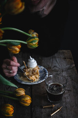 Woman eating piece of Mille-feuille cake decorated with meringues on vintage plate. Glass of coffee, candles and tulips  on old wooden table.