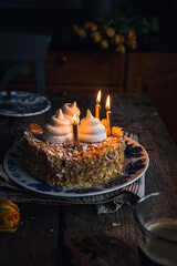 Mille-feuille cake decorated with meringues and three lit candles on vintage plate on old wooden table.