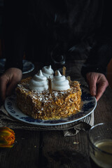 Woman holding Mille-feuille cake decorated with meringues and thin candles on vintage plate above  old wooden table.