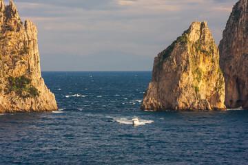 Fototapeta na wymiar Small tourist boat sailing between Faraglioni (huge rocky stacks), Capri, Italy
