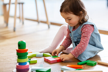childhood, leisure and people concept - little baby girl playing with wooden toy blocks on floor at home