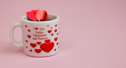 Happy Valentine`s Day greeting card.Holiday Valentine decoration.White glass cup with red glittering hearts on a pink background.Love or romantic concept with space for text. Selective focus.