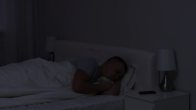 insomnia concept - disturbed thoughtful guy lying in bed alone in dark bedroom at night