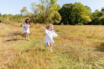 Naklejka na ściany i meble Blonde little girl runs across a field with grass. Wind in your hair.