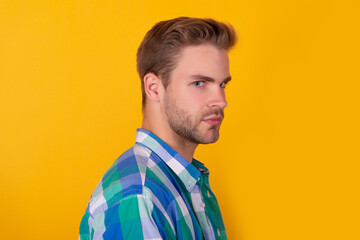 Handsome unshaven guy with serious face half turn yellow background, portrait