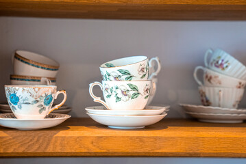 Floral hand painted porcelain teacups with saucers displaying on wooden shelves for sale, Ceramic flower pattern tea sets on shelves