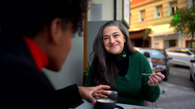 Positive ethnic woman drinking coffee and chatting with black friend