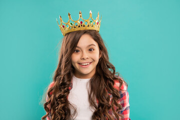 smiling child with curly hair in queen crown on blue background, smug