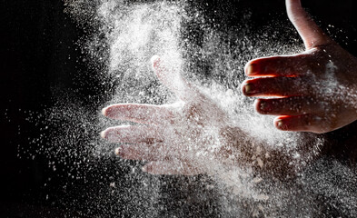 woman chef hand clap with splash of white flour and black background
