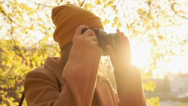 Lady photographer in warm hat takes picture with camera while standing in sunny autumn park on nice day close view slow motion