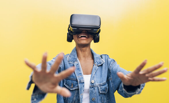 Smiling young woman wearing virtual reality headset gesturing against yellow background