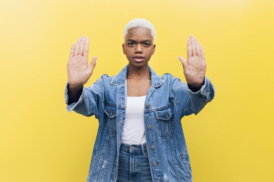 Woman showing stop gesture with both palms against yellow background