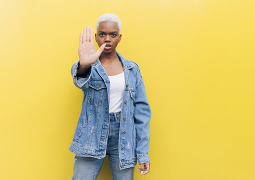 Serious woman making stop gesture standing against yellow background