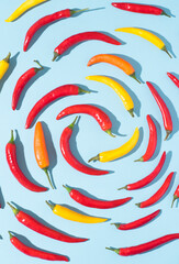 Hot chili dynamic pepper background in the form of a spiral. Hot red, yellow, orange peppers on blue, natural spices, top view, pop-art style with trendy dark shadows