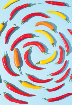 Fototapeta Hot chili dynamic pepper background in the form of a spiral. Hot red, yellow, orange peppers on blue, natural spices, top view, pop-art style with trendy dark shadows