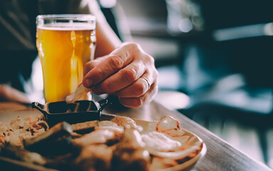 man hand with glass of cold beer and plate with snacks in bar or pub