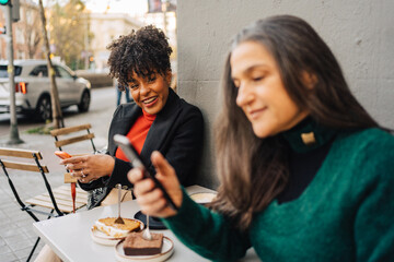 Cheerful black woman showing smartphone to ethnic friend