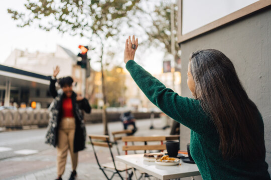 Ethnic woman waving hand to black friend walking on street
