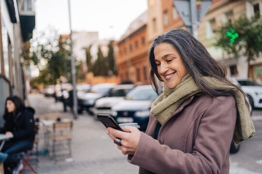 Smiling woman with coffee cup using smartphone on street