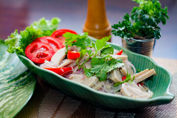 Spicy vietnamese sausages salad placed in a leaf-shaped green plate. With onion, garlic, red pepper on a black wooden table