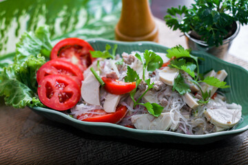 Spicy vietnamese sausages salad placed in a leaf-shaped green plate. With onion, garlic, red pepper on a black wooden table