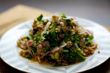 Ground pork salad placed in white and gray plates with onions, garlic, red chillies on a black wooden table.