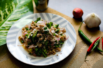 Ground pork salad placed in white and gray plates with onions, garlic, red chillies on a black wooden table.